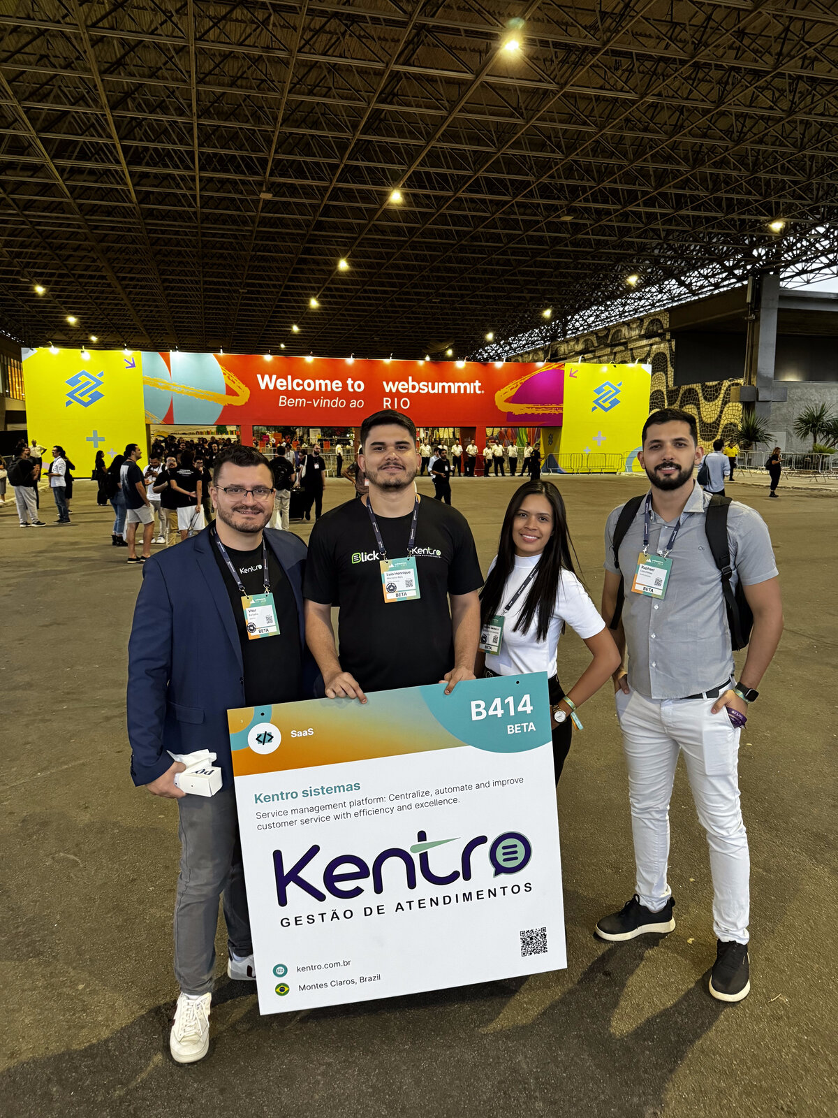 Equipe da Kentro no Web Summit Rio com placa de expositor